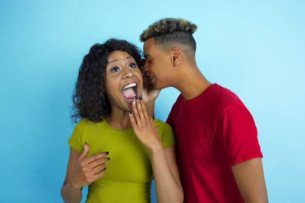 情侣听着秘密 她在笑年轻感性的非洲裔男女穿着蓝色背景的彩色衣服人类情感的概念 面部表情 关系 广告 友谊面部在一起选择