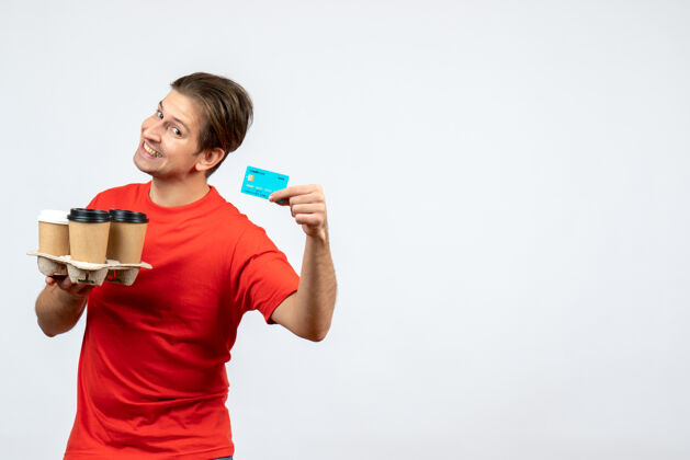 命令俯视图：一个身穿红色上衣 面带微笑 心情愉快的年轻人 手里拿着白墙上的银行卡肖像年轻人成人