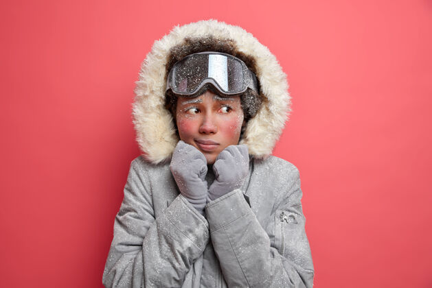 风帽美丽的冻僵的女人在寒冷的雪天和二月的低温中颤抖着穿着暖和的灰色夹克和滑雪镜去山上滑雪夹克外套颤抖