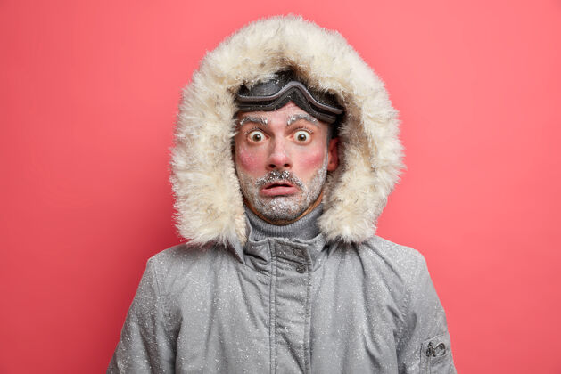 自然震惊的未刮胡子的男人穿着暖和的夹克 带风帽 非常适合寒冷的冬天 脸上覆盖着雪 不适应严寒的环境 积极休息娱乐人活动