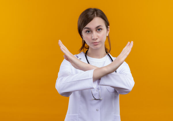 女性严肃的年轻女医生穿着医用长袍和听诊器在孤立的橙色空间和复印空间做停止手势复制年轻严重