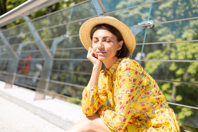 城市户外写真黄色夏装女子坐在桥上闭着眼睛 心情愉快 享受着阳光明媚的夏日旅游乐趣人