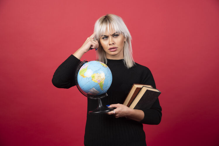 书房年轻的女模特在红墙上摆着一本书和一个地球仪年轻站立肖像