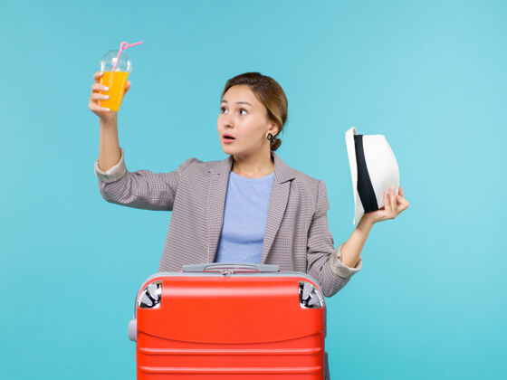 旅行正面图：度假中的女性拿着新鲜果汁和她的帽子在蓝色背景下航行海上度假人前面果汁