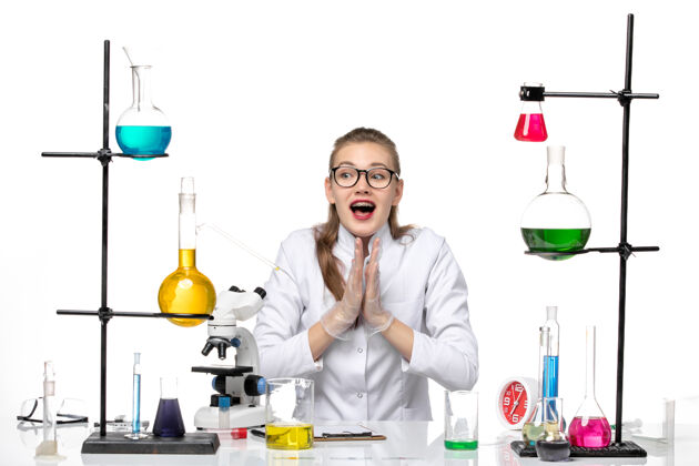 白色正面图：穿着医疗服的女化学家坐在白色办公桌上 拿着溶液化学大流行性冠状病毒研究实验室坐着