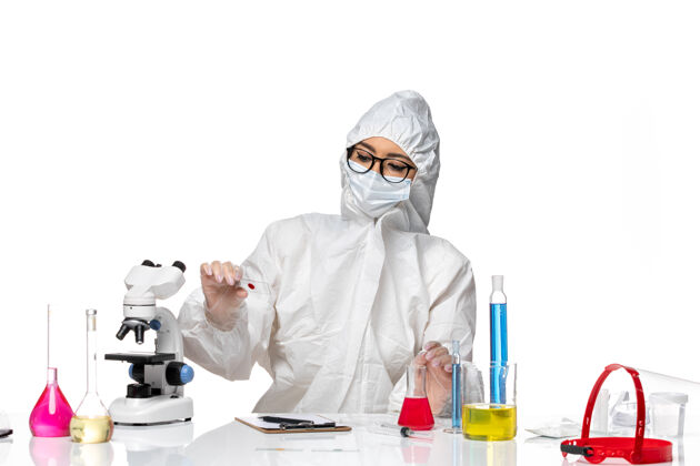 化学正面图：穿着特殊防护服的女化学家拿着样本坐在白色办公桌上化学冠状病毒大流行人保护男人