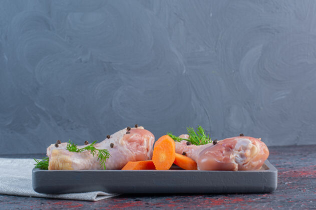 生的黑色的生鸡腿盘放在大理石表面烹饪蔬菜食物