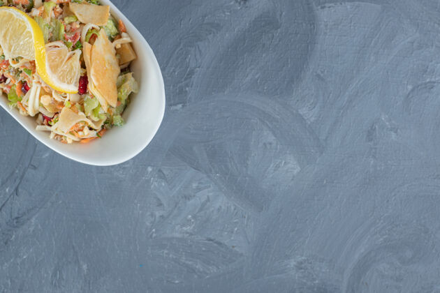 沙拉大理石桌上点缀着柠檬片的混合蔬菜沙拉切片顶视图美食