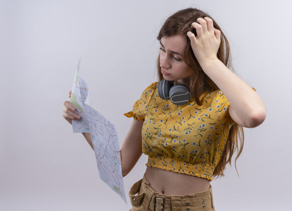 困惑迷茫的年轻女孩戴着耳机在脖子上 拿着地图 在孤立的空白处看着它年轻地图女孩