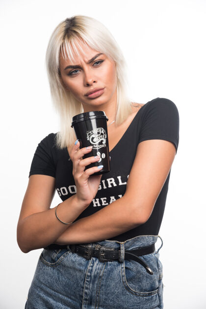 金发年轻女子拿着一杯咖啡站在白色的墙上 表情严肃姿势肖像严肃