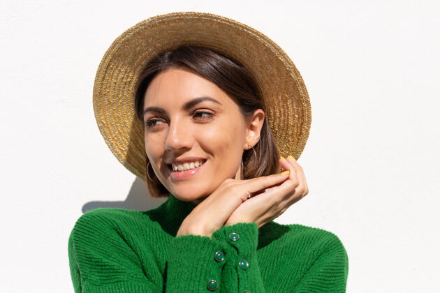 女性穿着绿色休闲毛衣和帽子的时尚女士户外白墙上平静自信的微笑爱好休闲肖像