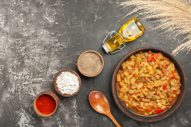 木头顶视图烤茄子沙拉碗 油瓶 木勺和不同的香料碗在黑暗的表面胡椒食物烤肉
