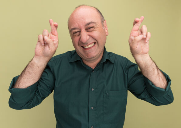 感觉微笑的中年男子穿着绿色t恤交叉手指隔离在橄榄绿的墙上手指表情人