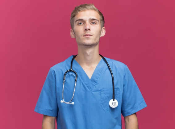 衣服自信地看着相机年轻的男医生穿着医生制服听诊器隔离在粉红色的墙上与复印空间年轻人感情人