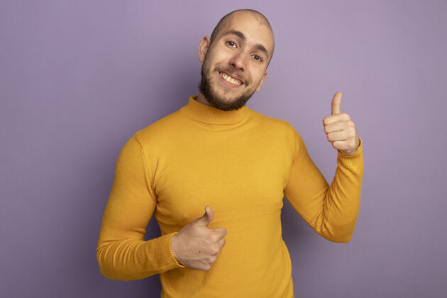 小伙子微笑的年轻帅哥竖起大拇指孤零零地站在紫色的墙上秀大拇指微笑