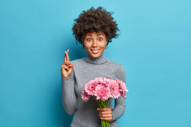 束积极的非裔美国人的肖像十字架手指相信梦想成真持有粉红色非洲菊花束浪漫开花庆祝
