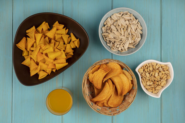 视图顶视图美味的脆薯片放在一个桶里 白色的葵花籽放在一个碗里 松子和一杯橙汁种子薯片食物