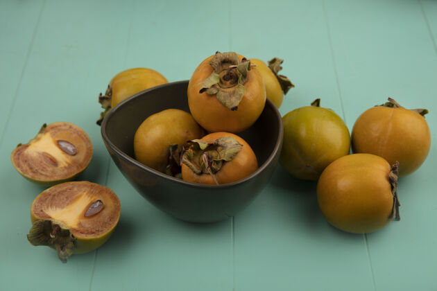 蓝色顶视图橙色未成熟的柿子水果与柿子水果隔离在一个蓝色的木桌碗生新鲜木头