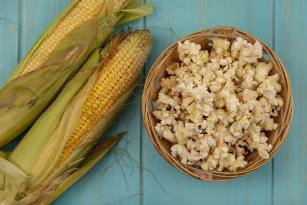 食物蓝色木桌上的桶上有头发和爆米花的有机健康玉米的顶视图玉米顶部新鲜