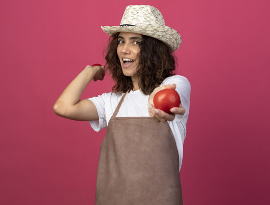 大笑穿着制服的年轻女园丁 戴着园艺帽 手里拿着粉红色的西红柿西红柿园艺年轻