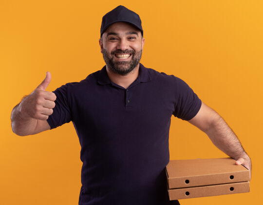 制服微笑的中年送货员穿着制服 戴着帽子 拿着披萨盒 在黄色的墙上孤立地竖起大拇指微笑盒子拇指
