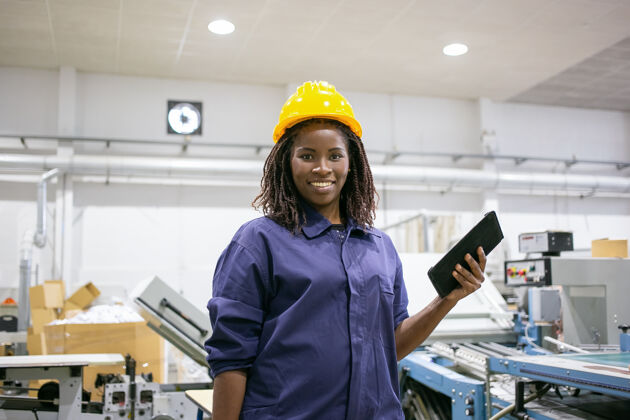 技师快乐的工厂女工戴着安全帽 站在机器前 手持平板电脑 面带微笑地看着前方女性快乐劳动