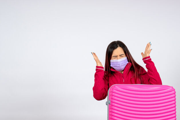 度假正面图年轻女性带着粉红色的袋子在白墙上戴着口罩病毒度假柯维德大流行旅行的女人肖像病毒风景
