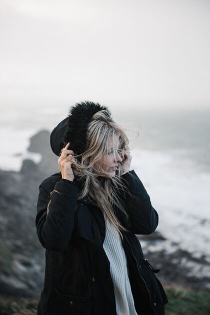 肖像年轻的金发女郎戴着帽子 在多风的天气里走在多岩石的海岸上自然天气年轻