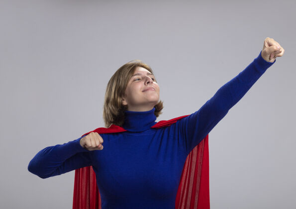 超级英雄穿着红色斗篷的年轻金发女超人举起拳头站在超人的姿势看着她孤立在白墙上的拳头感情超人女孩