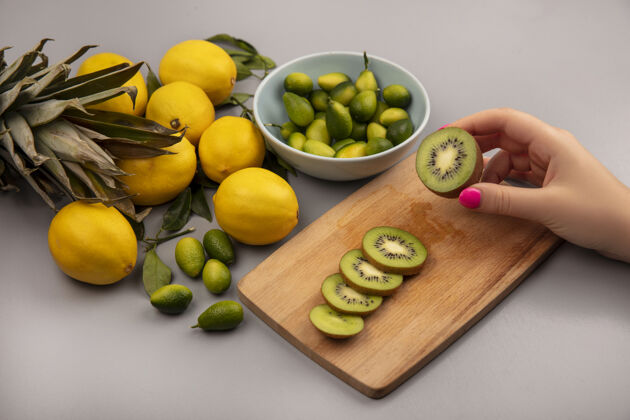 新鲜女性手拿新鲜猕猴桃在木制厨房板上的俯视图 碗上放着金盏花 柠檬被隔离在白色背景上手板水果