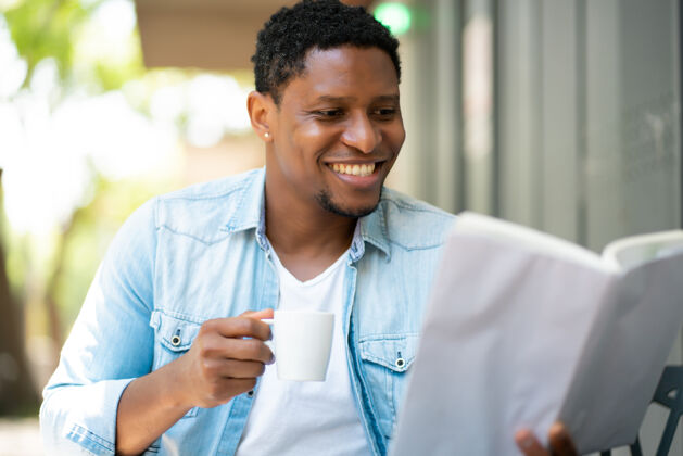 年轻一个非洲裔美国人坐在咖啡馆里放松和看书男性喝酒欢乐
