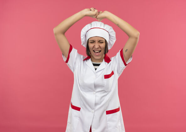 拳头快乐的年轻女厨师穿着厨师制服举起拳头闭上眼睛孤立在粉红色欢乐年轻制服