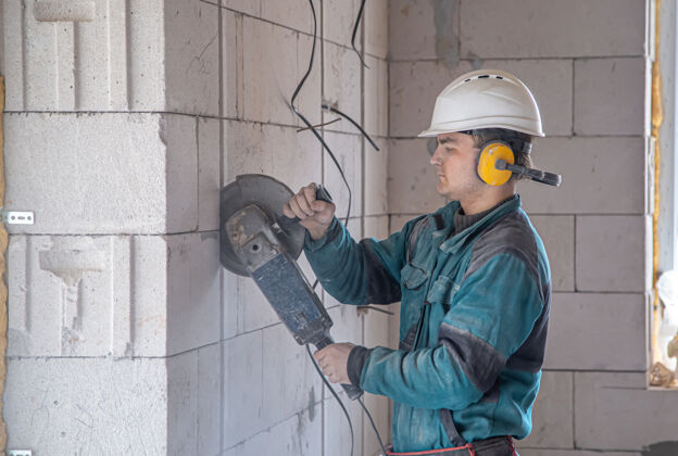 工作勤杂工在工地用磨床切割的过程中建筑场地建筑头盔