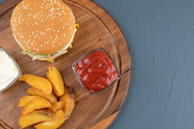 番茄酱土豆薯条配番茄酱和蛋黄酱 旁边是蓝色背景的木板上的汉堡包高品质照片一餐快餐薯条