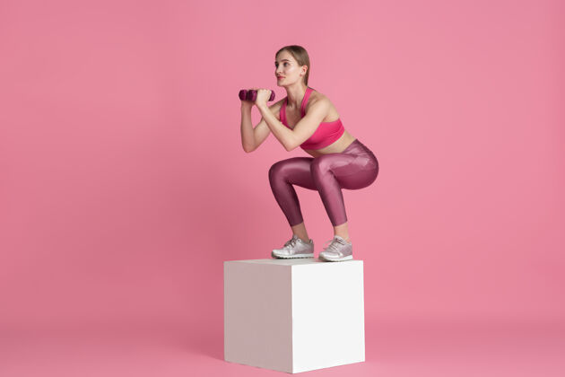 举重美丽的年轻女运动员在粉红色墙上练习单色肖像体重运动装杠铃