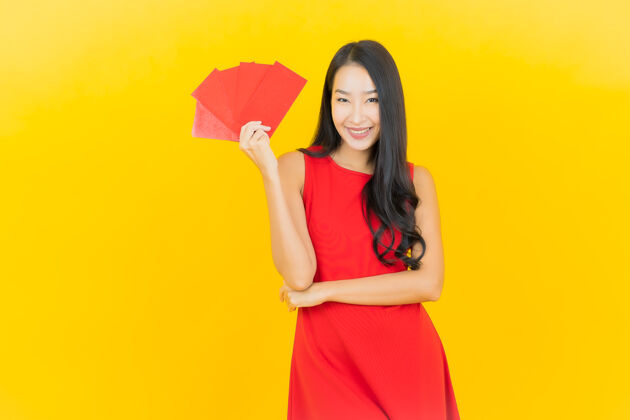 庆祝在黄色的墙上画一幅美丽的亚洲年轻女子拿着中国新年的红包亚洲年轻东方