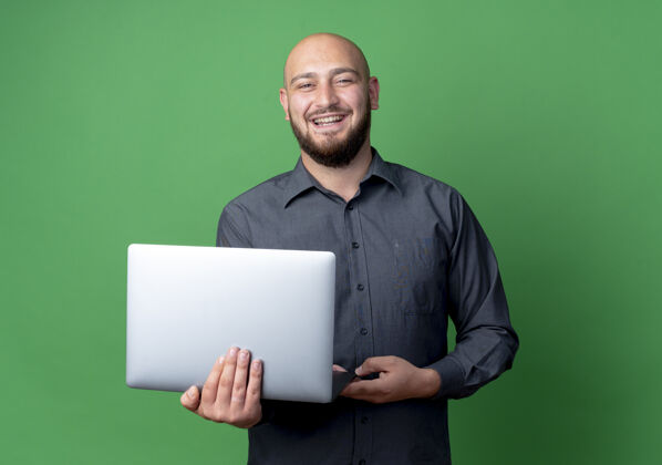 男人快乐的年轻秃头呼叫中心男子手持笔记本电脑隔离在绿色笔记本电脑持有喜悦