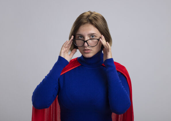 超级英雄穿着红斗篷的年轻金发女超级英雄戴着眼镜望着前面 触摸着隔离在白墙上的眼镜人金发感情