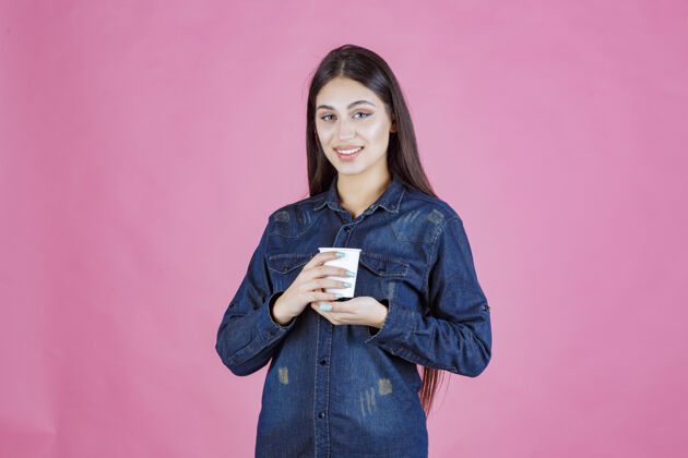 茶穿着牛仔衬衫的女孩正在享受一杯一次性咖啡休闲姿势温暖