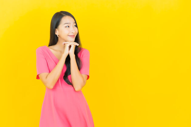 快乐黄色墙壁上 美丽的亚洲年轻女子身着粉色连衣裙微笑的画像肖像生动年轻