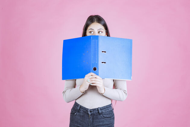 女性女孩拿着一个蓝色的项目文件夹 把她的脸藏在后面报告姿势装备