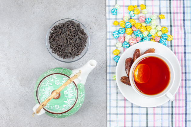 水果茶壶 一小碗茶叶和一杯茶放在毛巾上 大理石背景上撒着爆米花糖高质量的照片爆米花茶杯枣