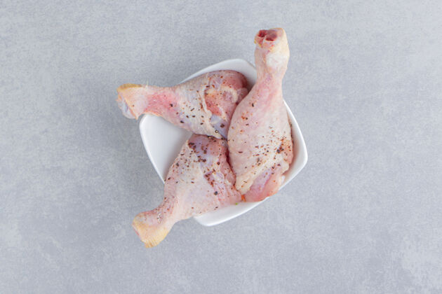 美味新鲜的鸡腿在碗里 在蓝色的表面上鸡腿生的肉