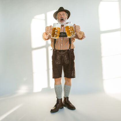 巴伐利亚啤酒节高级男士的肖像 戴着帽子 穿着传统的巴伐利亚服装在白色背景的摄影棚拍摄的男性全长庆祝 节日 节日的概念喝啤酒巴伐利亚节日酒馆