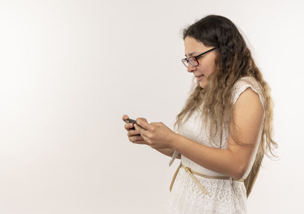 眼镜年轻漂亮的女学生戴着眼镜 背着书包站在侧视图中 用手机隔离在背景上 留有复印空间包漂亮年轻