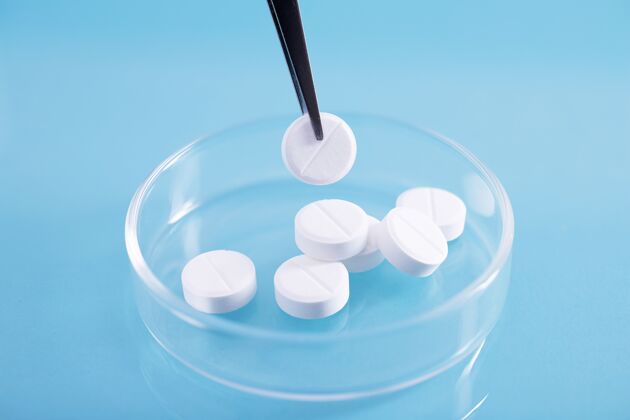 健康特写镜头镊子拿起一堆白色药丸在一个实验室的玻璃盘药物治疗医学
