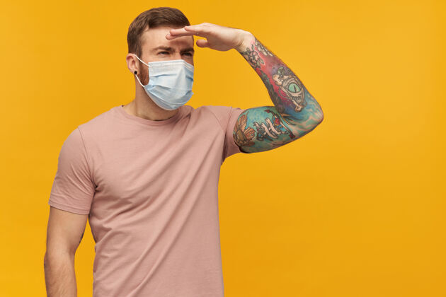 流感一个留着胡须 纹身 穿着粉色T恤 脸上戴着防病毒面具 脸上挂着黄色墙壁上的冠状病毒的沉思的年轻人年轻医学流行病