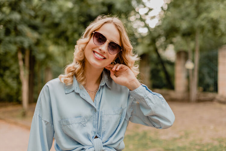 女人迷人的金发微笑的女人穿着时髦的服装在公园散步休闲手提包包