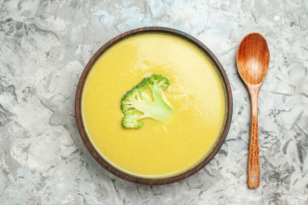 热的近距离观看奶油西兰花汤在一个棕色的碗和勺子在灰色的桌子上晚餐勺子烹饪