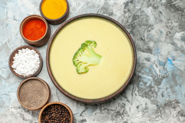汤碗上图：棕色碗里的奶油西兰花汤和灰色桌子上的不同香料餐健康汤
